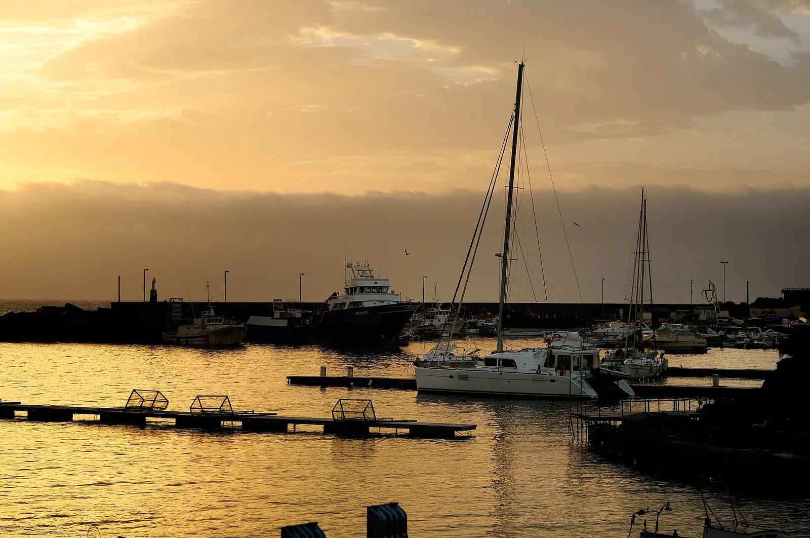 Un porto turistico all'alba, con una barca a vela ormeggiata a un pontile galleggiante e altre barche sullo sfondo